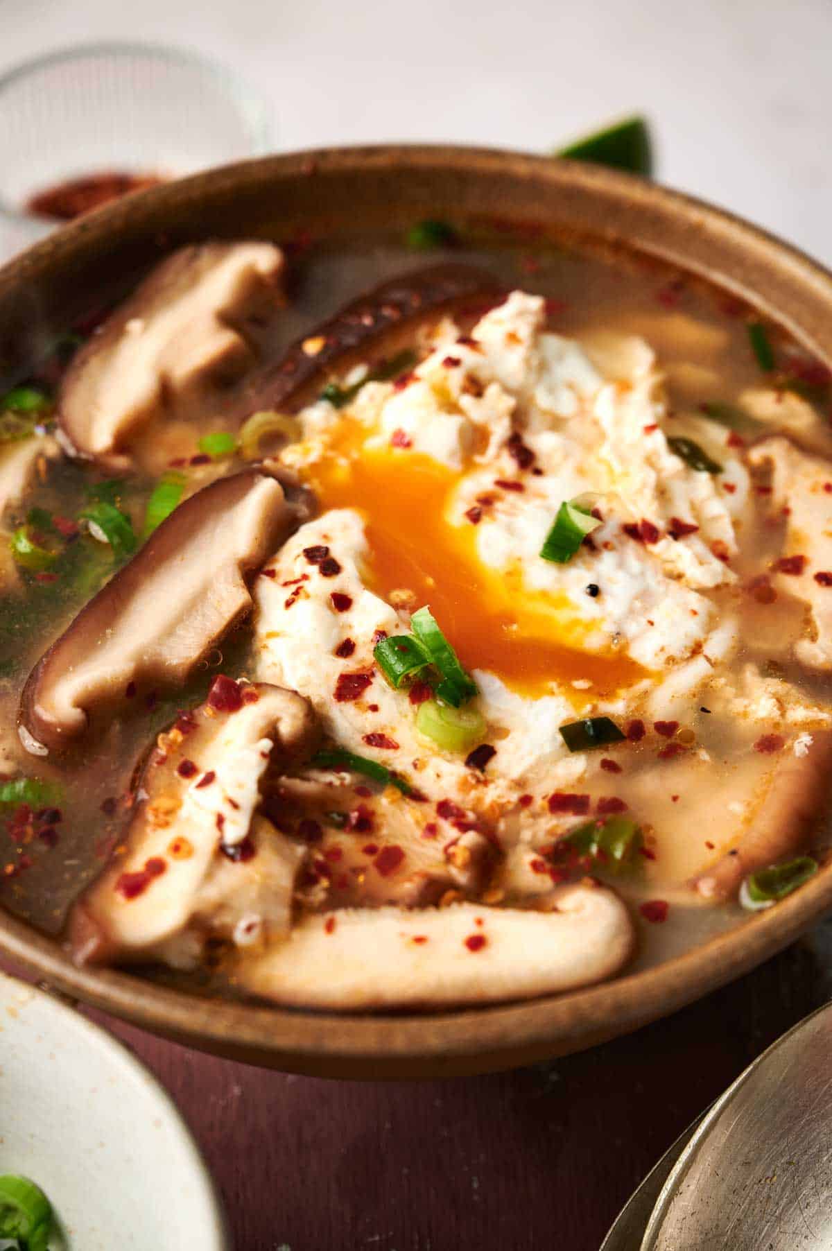 A bowl of Korean tofu soup with vegetables and eggs.