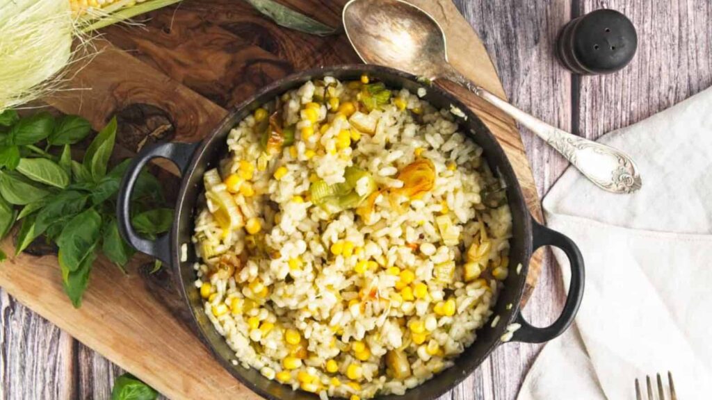 A skillet filled with corn and rice on a wooden cutting board.