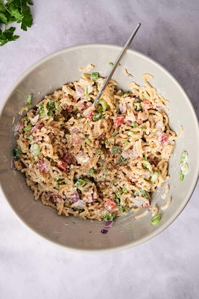 A bowl of macaroni salad with red onions, celery, and herbs, mixed together and served in a white bowl with a fork.