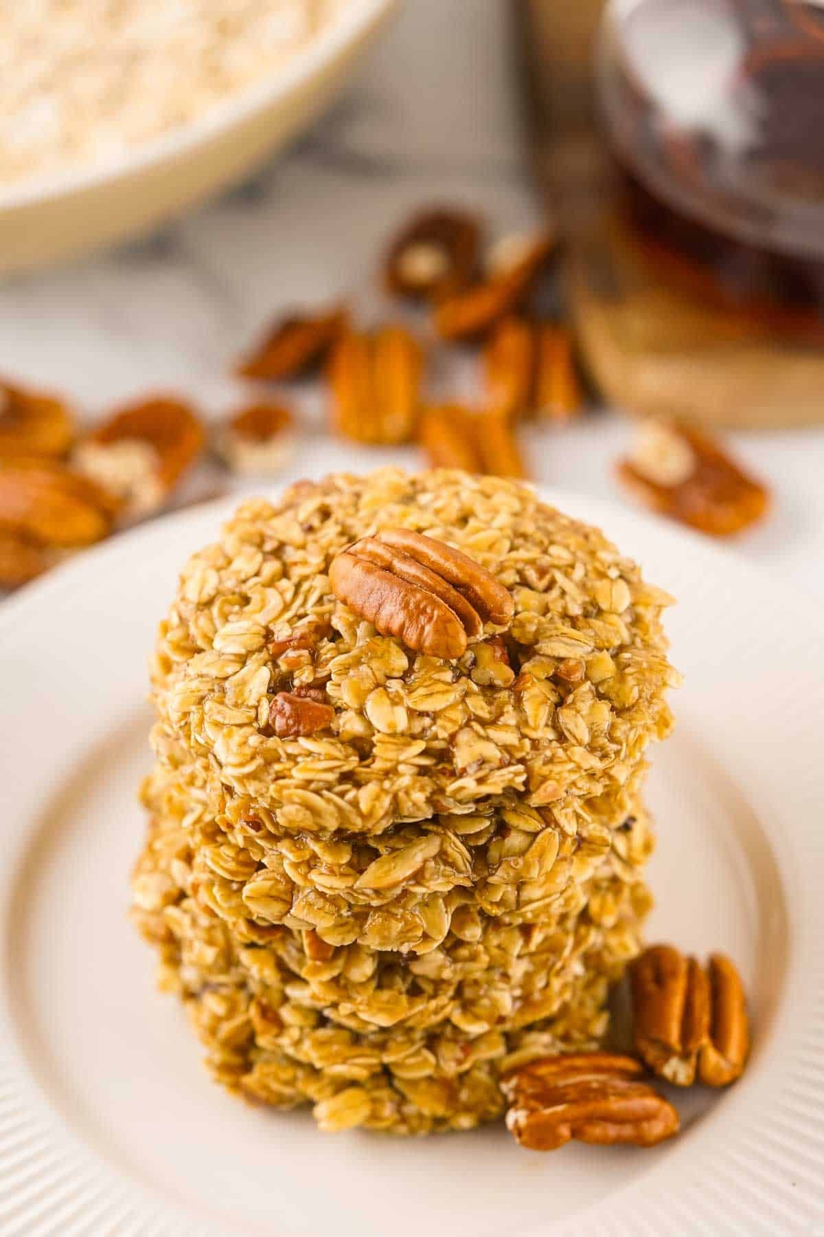 A stack of no-bake maple pecan cookies, placed on a white plate with more pecans scattered around, and a jar of honey in the background.
