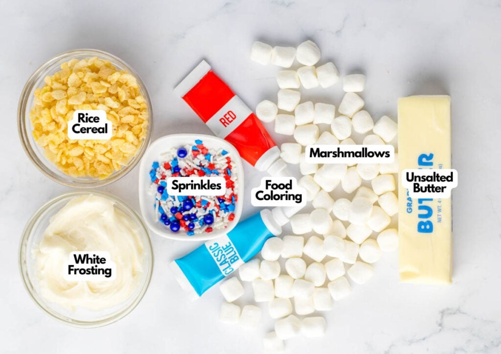 Ingredients for Patriotic Rice Crispy Treats on a white surface: rice cereal, white frosting, sprinkles, red and blue food coloring, mini marshmallows, and a stick of unsalted butter.