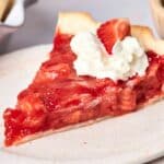 A slice of scrumptious strawberry pie, crowned with a dollop of fluffy whipped cream, sits invitingly on a pristine white plate.