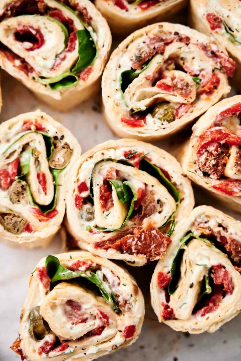 Close-up view of several pinwheel sandwiches filled with ingredients like spinach, roasted red peppers, sundried tomatoes, and cream cheese.