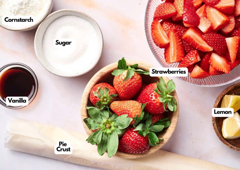 Ingredients for a homemade strawberry pie&mdash;cornstarch, sugar, chopped strawberries, vanilla, whole strawberries, pie crust, and lemon wedges&mdash;are neatly arranged on a countertop.
