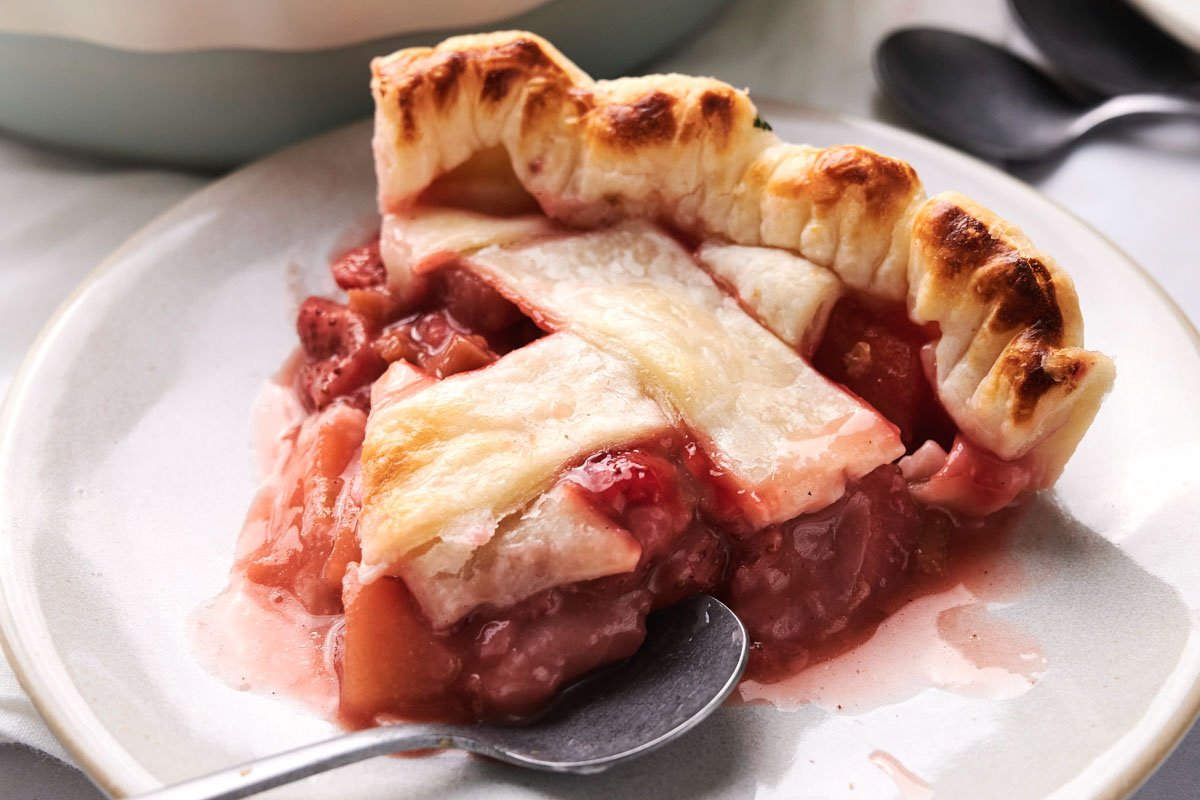 Slice of strawberry pie on a plate with two black spoons beside it.
