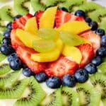 Close-up of a colorful fruit tart topped with sliced kiwi, strawberries, blueberries, and mango, arranged in concentric circles.