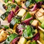 Close-up of grilled veggie skewers featuring zucchini, red onion, eggplant, and green bell pepper, all garnished with fresh herbs.