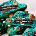 Close-up of Cookie Monster cookies, each featuring a chocolate sandwich cookie and chocolate chip pieces inside. The blue-colored cookies are stacked, revealing their cross-sections.