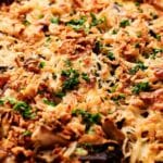 A close-up view of a baked air fryer mushroom casserole topped with crispy, shredded potatoes, melted cheese, and garnished with chopped parsley.