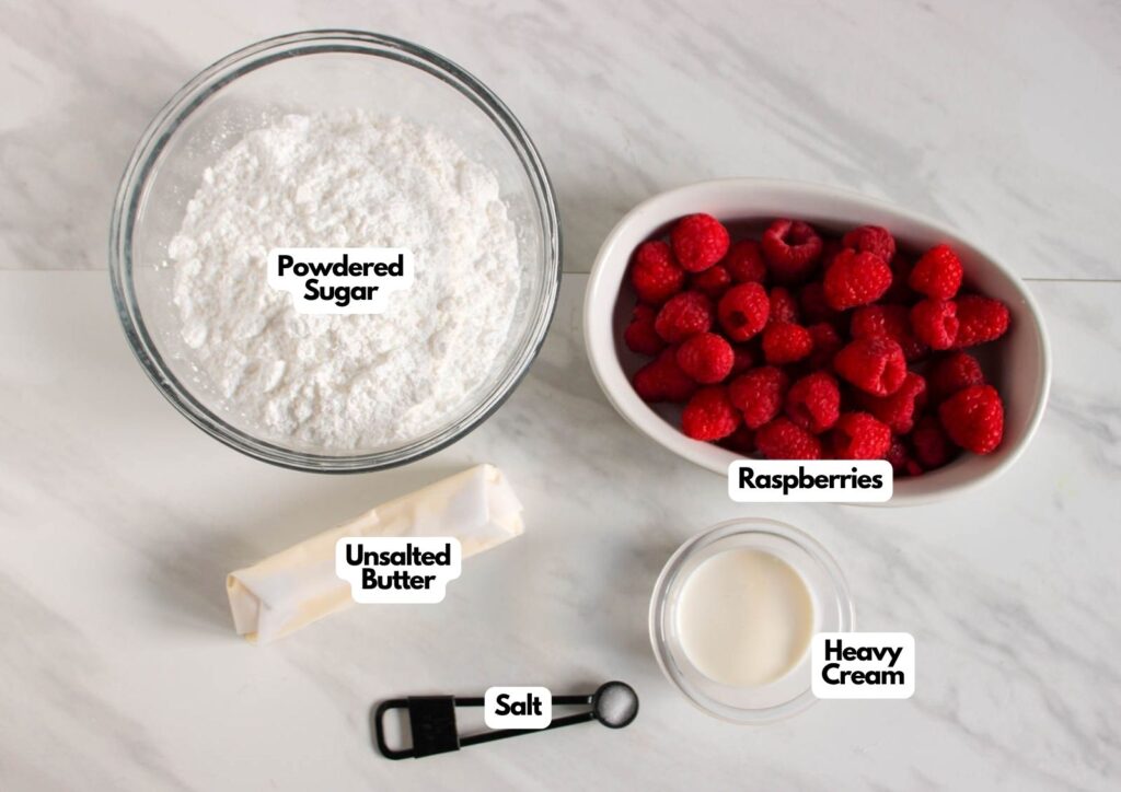 A bowl of powdered sugar, a dish of raspberries, a stick of unsalted butter, a spoon of salt, and a small bowl of heavy cream on a white surface—perfect ingredients for making Lemon Cupcakes with Raspberry Buttercream Frosting.