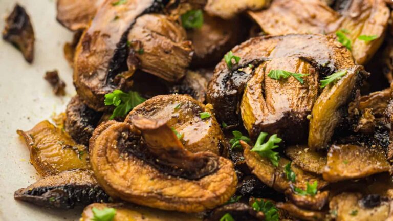 Close-up of sautéed mushrooms garnished with chopped parsley on a plate.