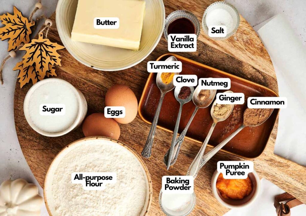 A wooden board displays labeled baking ingredients&mdash;perfect for Pumpkin Spice Roll Cookies&mdash;such as butter, vanilla extract, salt, sugar, eggs, all-purpose flour, baking powder, turmeric, clove, nutmeg, ginger, cinnamon, and pumpkin puree.