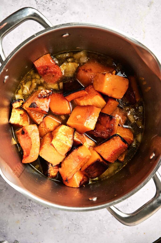 A pot filled with roasted butternut squash chunks, partially submerged in a savory broth, perfect for making a rich butternut squash soup.