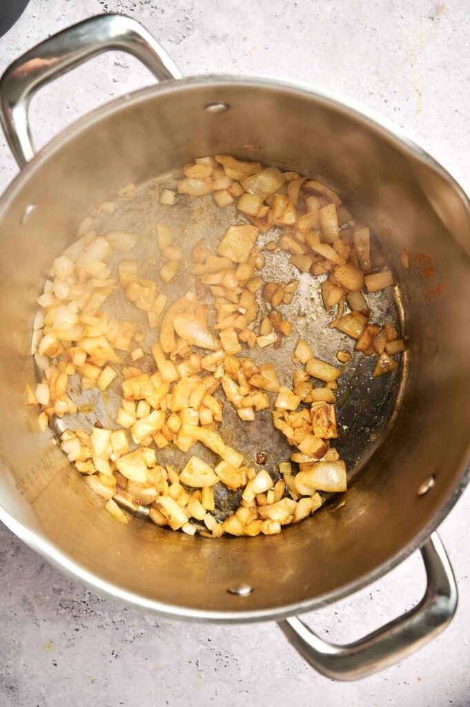Diced onions saut&eacute;ing in a large metal pot on a stovetop, the perfect base for a rich Butternut Squash Soup.