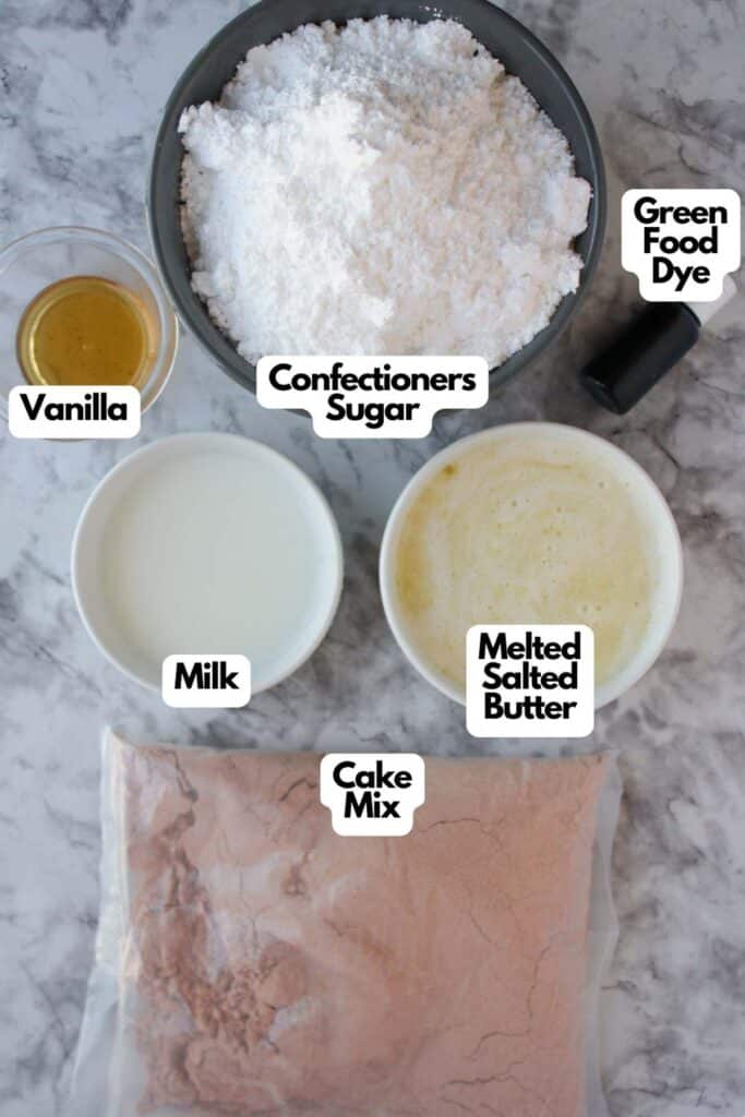 Ingredients for Festive Christmas Tree Cupcakes on a marble surface include confectioners sugar, green food dye, vanilla, milk, melted salted butter, and cake mix.