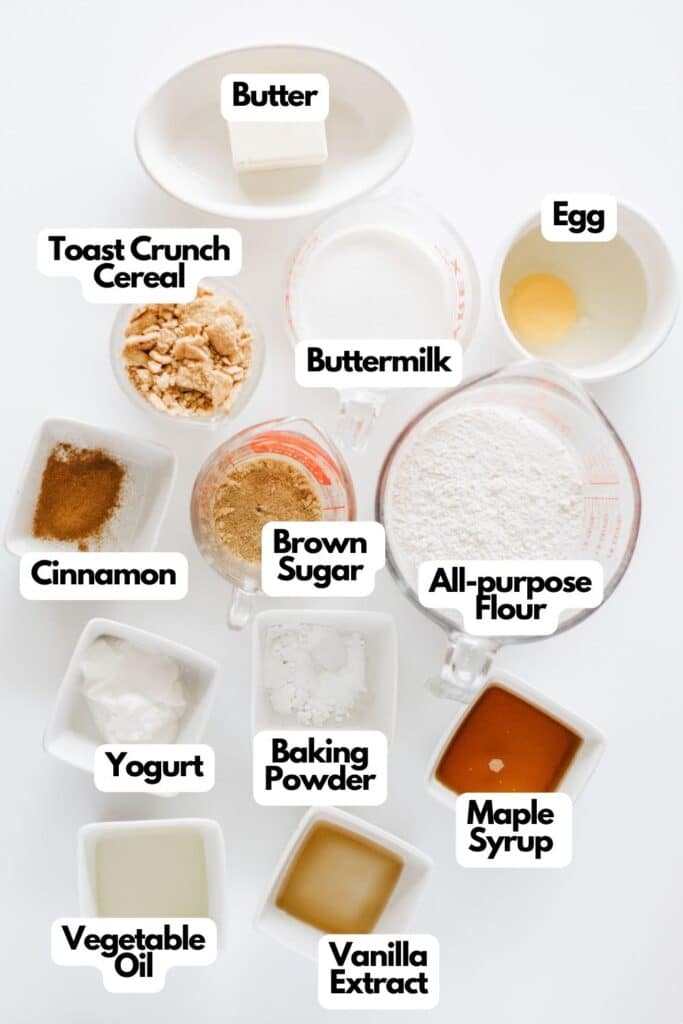 Ingredients for making Glazed Cinnamon Crunch Toast Donuts, including butter, buttermilk, toast crunch cereal, egg, all-purpose flour, brown sugar, cinnamon, yogurt, vegetable oil, maple syrup, baking powder and vanilla extract arranged on a white surface.