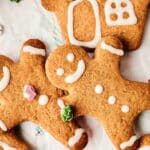 Three meticulously decorated gingerbread cookies, including two smiling gingerbread men and an intricately designed house, all adorned with white icing detailing, set against a pristine white background.