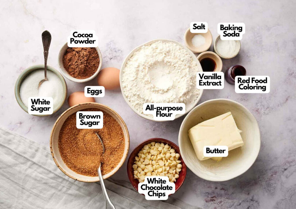 Baking ingredients for Copycat Crumbl Red Velvet White Chip Cookies, including all-purpose flour, sugars, cocoa powder, eggs, white chocolate chips, butter, salt, baking soda, vanilla extract, and red food coloring.