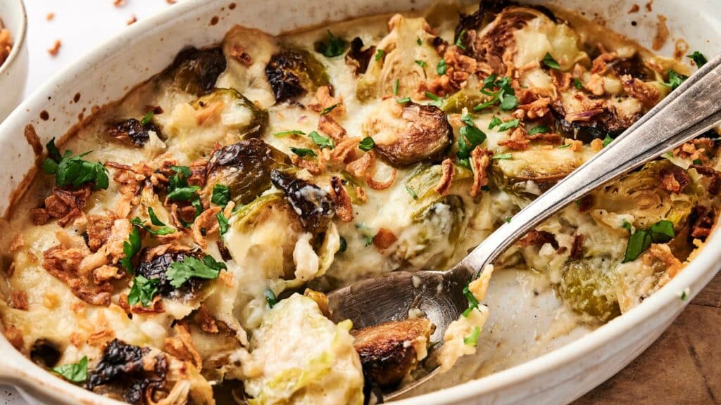 Casserole dish with Brussels sprouts, crispy onions, cheese, and herbs, mixed with a spoon.