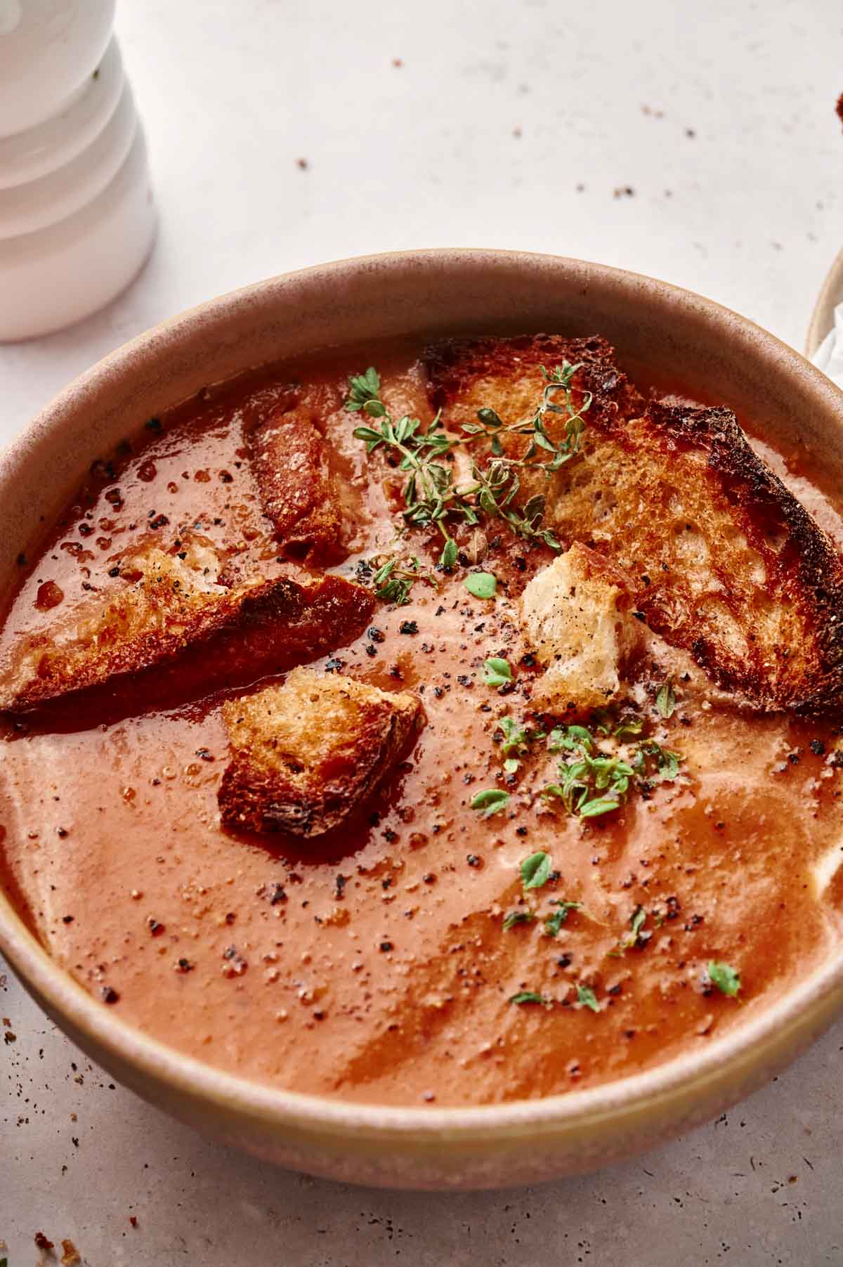 A bowl of roasted tomato bisque garnished with croutons, fresh herbs, and ground pepper.