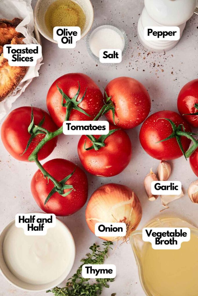 A top-down view of various ingredients for Roasted Tomato Soup labeled: tomatoes, garlic, onion, thyme, toasted slices, salt, pepper, olive oil, half and half, and vegetable broth arranged on a kitchen counter.