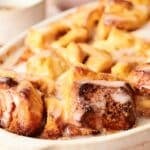 A baking dish filled with glazed, golden-brown pastry pieces, likely cinnamon rolls or a similar dessert.