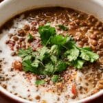 A steaming bowl of lentil soup garnished with fresh cilantro, a swirl of cream, and aromatic spices.