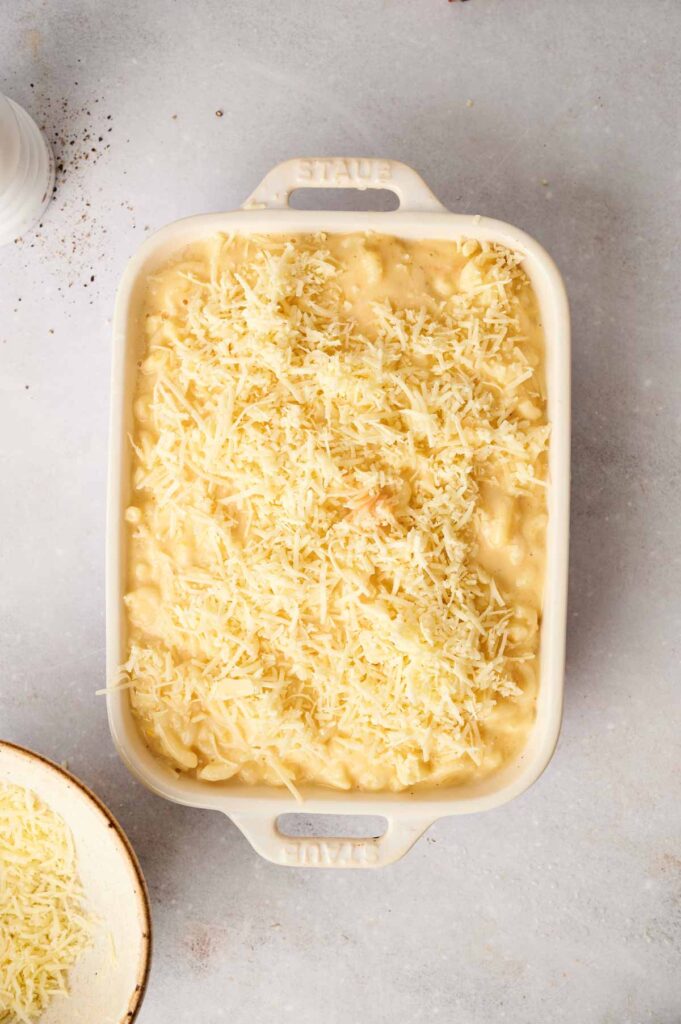 A baking dish filled with creamy Butternut Squash Mac and Cheese is topped with shredded cheese, resting enticingly on a light gray surface.