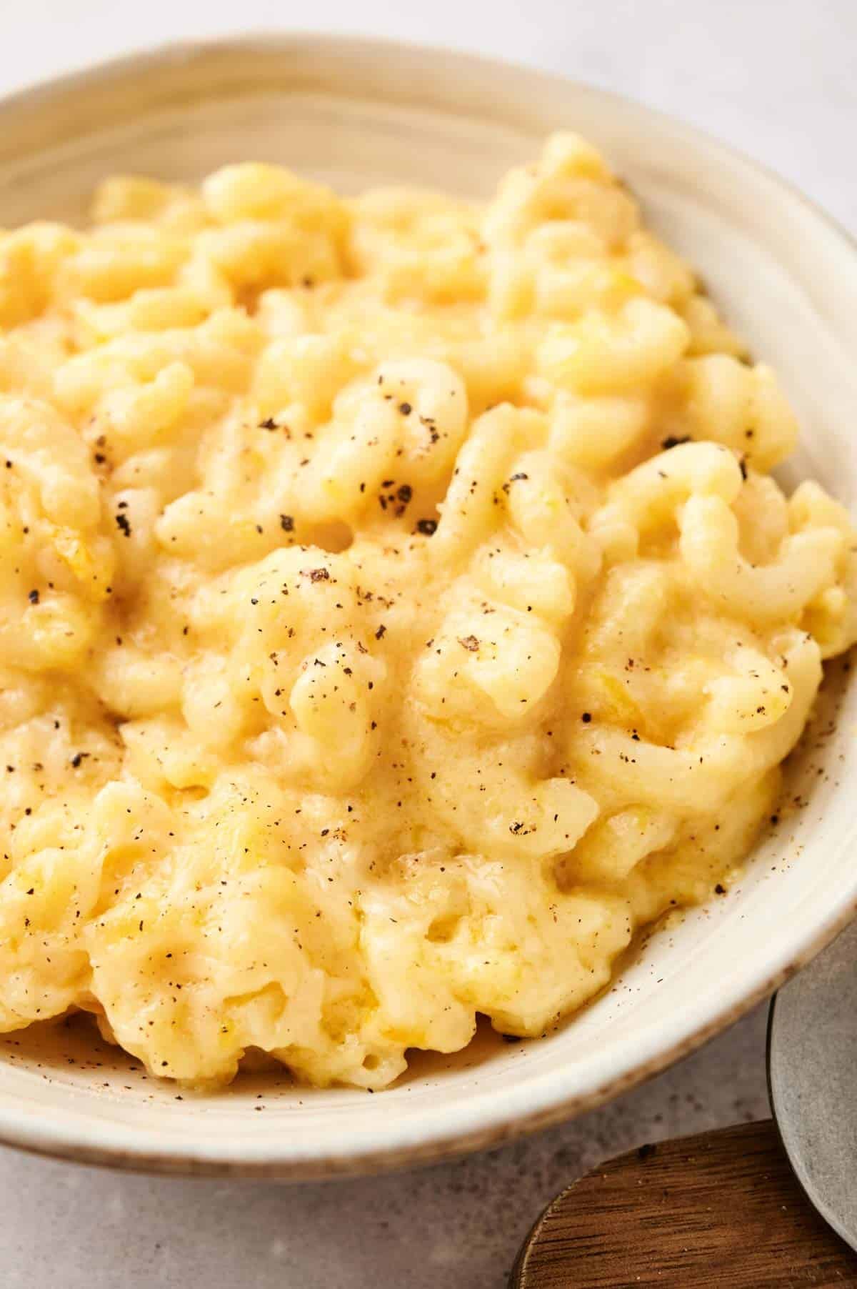 A bowl of creamy butternut squash mac and cheese topped with a sprinkle of black pepper.