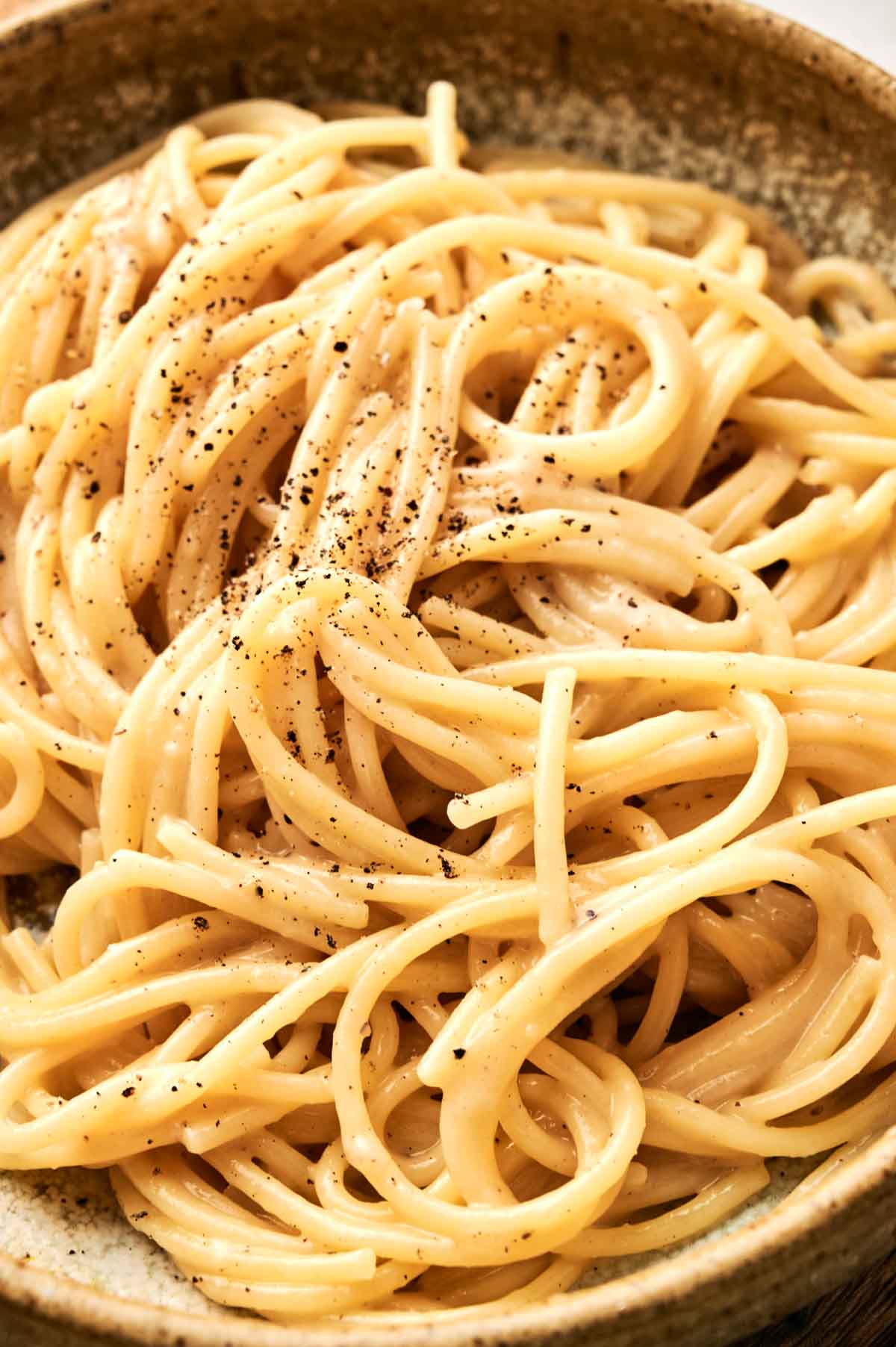 A close-up of a plate of spaghetti, reminiscent of traditional Cacio e Pepe, coated in a creamy sauce and adorned with cracked black pepper.