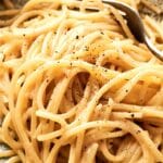 A close-up of Cacio e Pepe, showcasing cooked spaghetti noodles adorned with a fork and a sprinkle of black pepper.