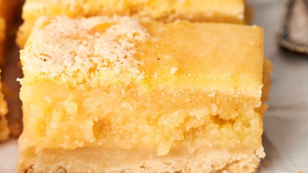 Close-up of lemon bars with a crumbly top and pale yellow filling.