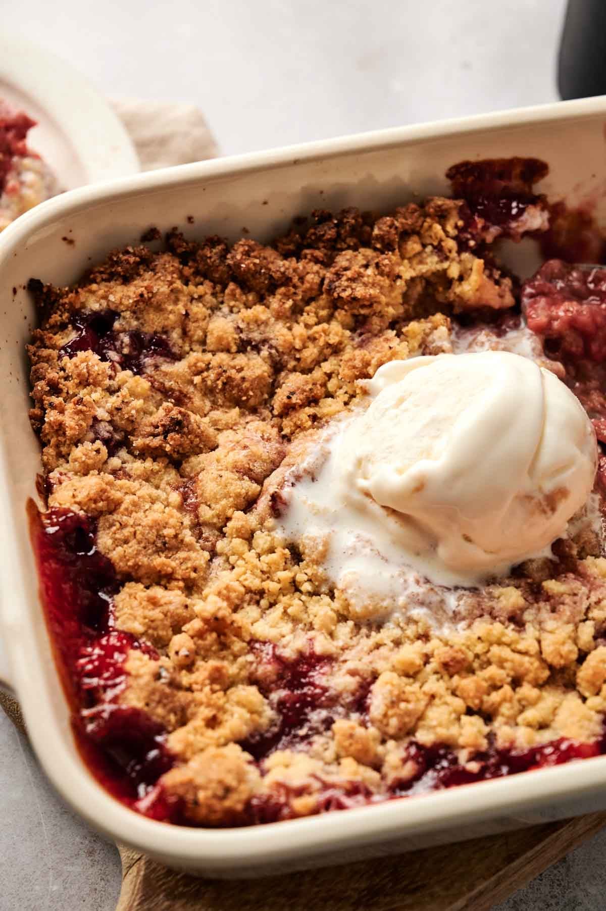 A baking dish with a delightful berry crumble, reminiscent of a strawberry dump cake, topped with a scoop of creamy vanilla ice cream.