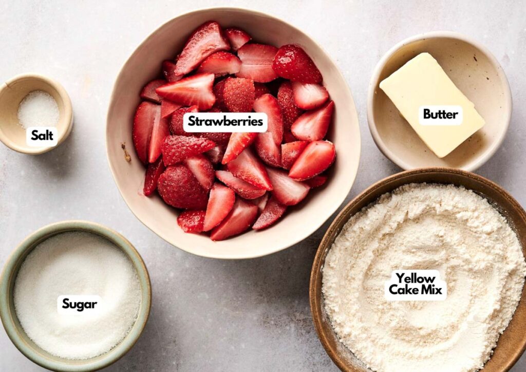 Bowls containing salt, sugar, sliced strawberries, butter, and yellow cake mix&mdash;perfect for making a strawberry dump cake&mdash;are arranged on a light surface, each ingredient labeled.