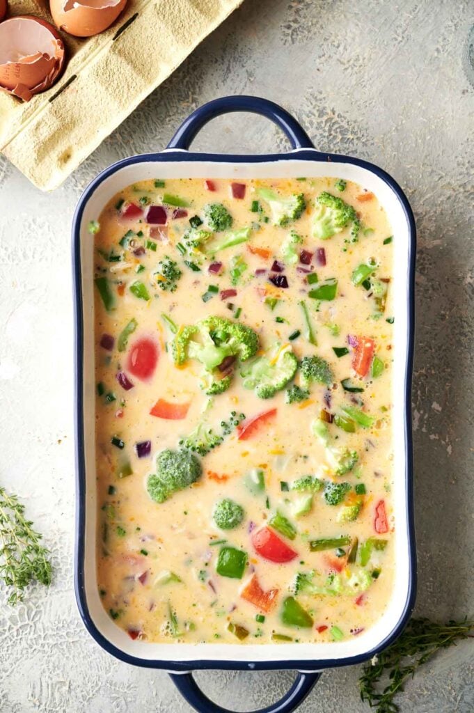 Overhead shot of unbaked egg casserole in a baking dish, filled with broccoli, bell peppers, and red onion in a creamy egg mixture.