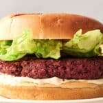 A close-up of a copycat Impossible Burger with a juicy beef patty, fresh lettuce, and creamy mayonnaise nestled in a soft bun.