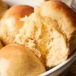 Golden-brown dinner rolls in a baking dish, with one roll partially broken open, revealing a soft, fluffy interior—this mouthwatering delight is the perfect dinner roll recipe for any occasion.