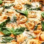 Close-up of tortellini in a creamy tomato sauce, reminiscent of a rich tortellini soup, garnished with spinach and fresh basil leaves.