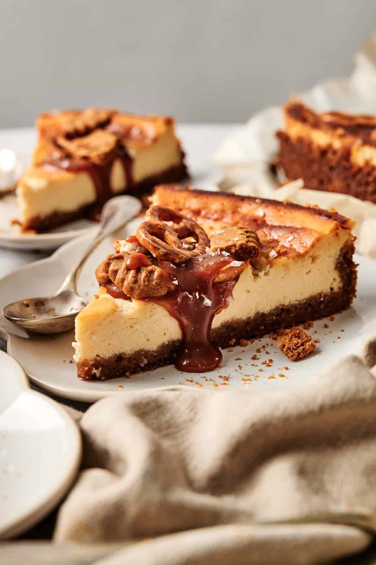 Slice of cheesecake topped with caramel, pecans, and a graham cracker crust on a plate with a spoon.