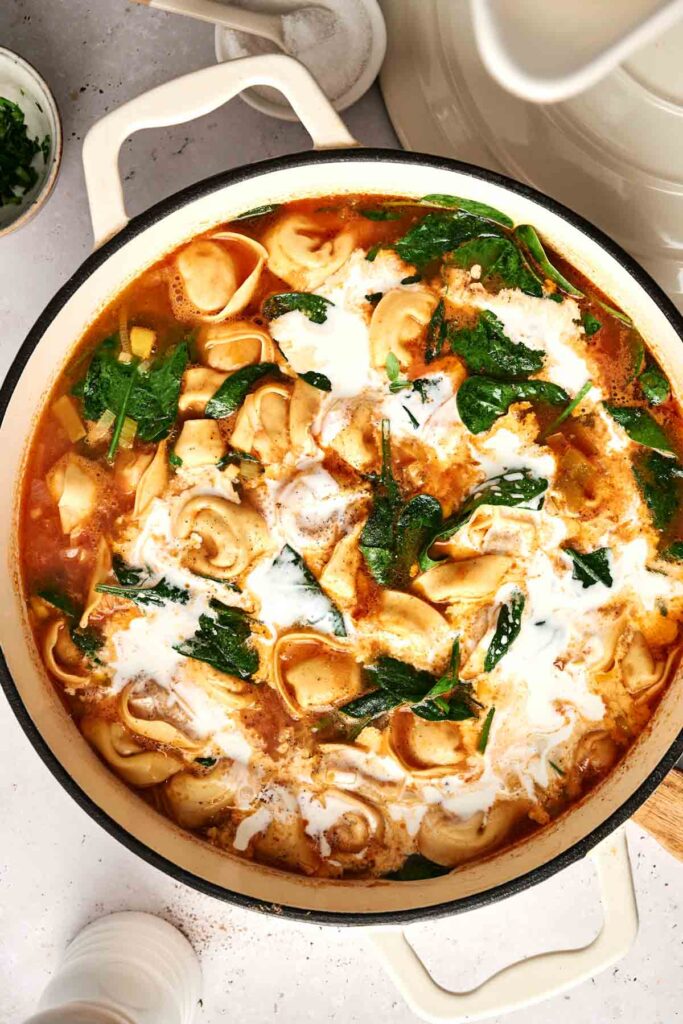 A pot of luscious tortellini soup with tender spinach submerged in a rich, velvety broth, elegantly garnished with a drizzle of cream.