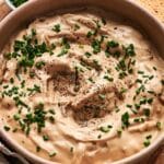 A bowl of creamy French onion dip, garnished with chopped chives and a sprinkle of black pepper.