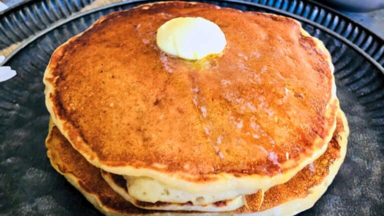 A stack of three pancakes with a pat of butter on top, placed on a dark plate.