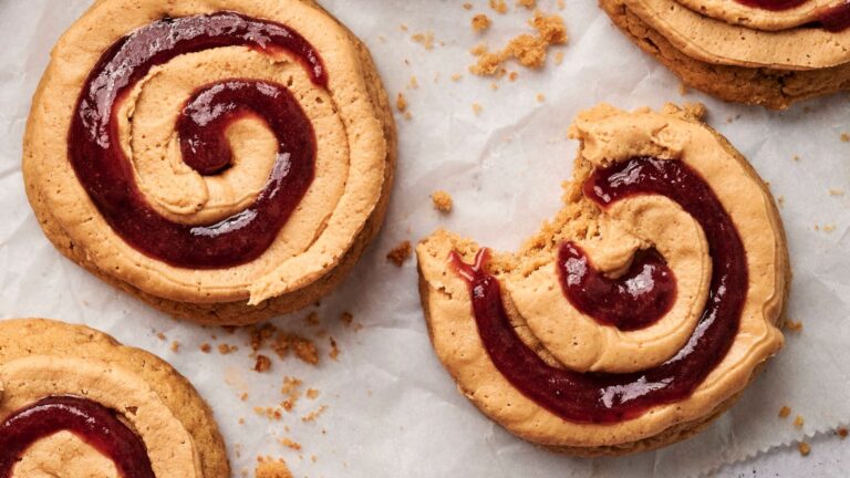 Swirled cookies with a red jam pattern on parchment paper, one cookie partially eaten.