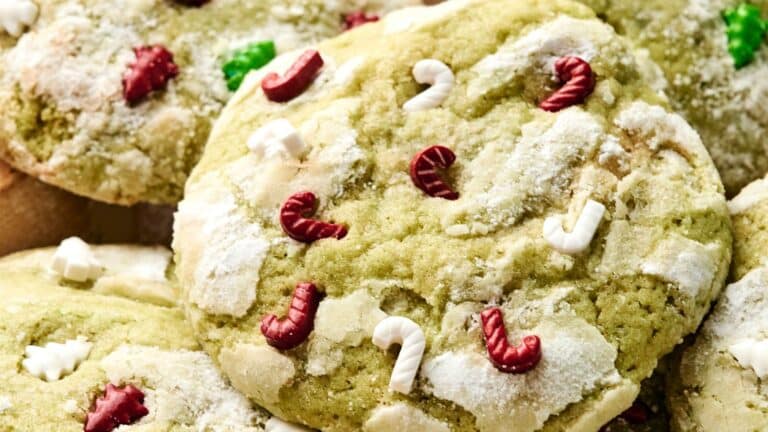 Close-up of green cookies topped with red and white candy cane-shaped sprinkles and dusted with powdered sugar.