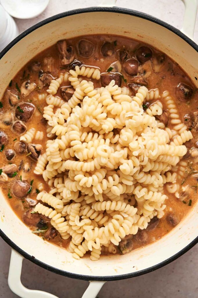 A pot of mushroom pasta with a creamy sauce is cooked to perfection, ready for mixing.