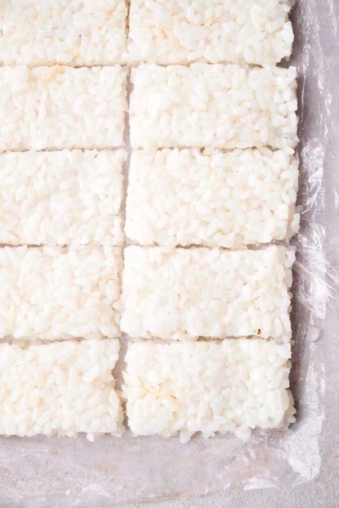 Rectangular portions of white, crispy rice are neatly arranged in rows on a clear plastic sheet.