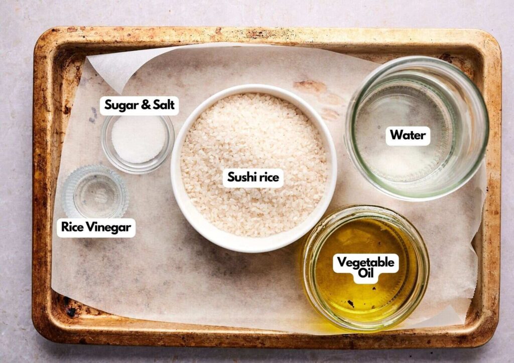 A tray holding labeled bowls of sushi rice, water, vegetable oil, rice vinegar, and a small dish of sugar and salt—everything you need to create perfect Crispy Rice at home.