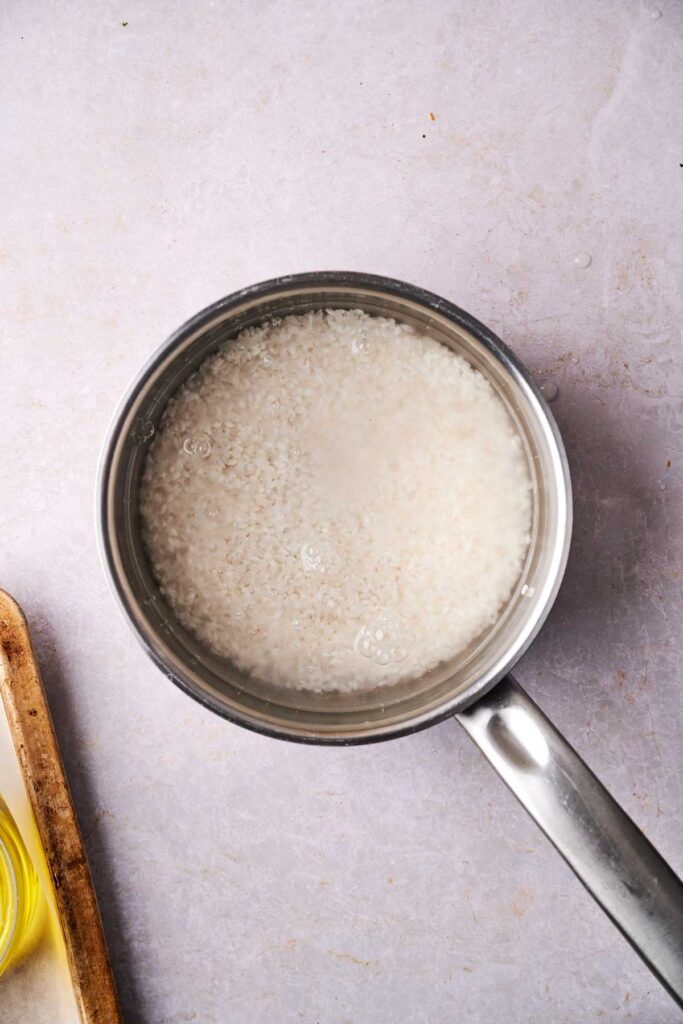 A pot filled with water and uncooked rice sits on a light-colored surface, hinting at the promise of crispy rice. A cutting board with a small bowl is partially visible on the left.