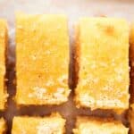 Close-up of neatly arranged, rectangular lemon bars with a light dusting of sugar on top, showcasing the golden perfection achieved by using an air fryer, all placed on a parchment-lined surface.