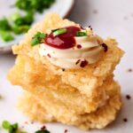 Crispy Rice squares stack up as the perfect base for a layer of creamy goodness, adorned with red sauce and a sprinkle of chopped green onions, all elegantly surrounded by scattered pieces for that delightful crunch.